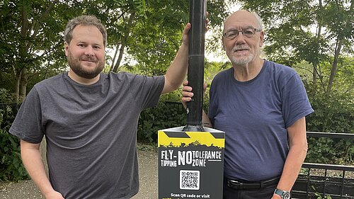 Liberal Democrat campaigners Alex Lewis and Alan Jones standing by a new fly-tipping sign